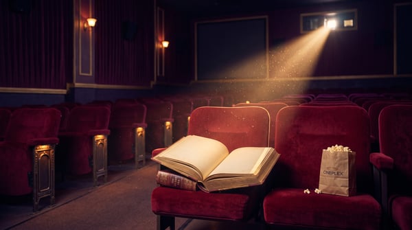 Open book and popcorn on velvet cinema seats beneath a warm projector beam
