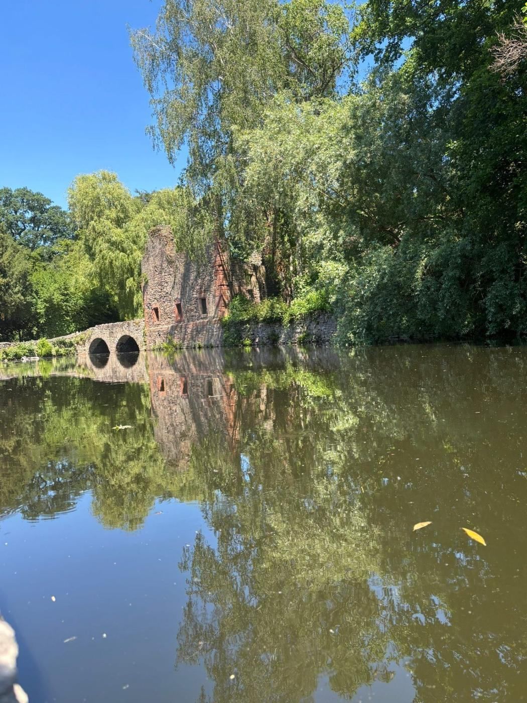 A stone ruin reflected in the calm river water of Schöntal Park in Aschaffenburg on a bright summer day