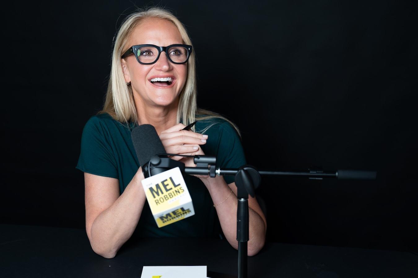 Mel Robbins laughing in front of a microphone on the set of The Mel Robbins Podcast